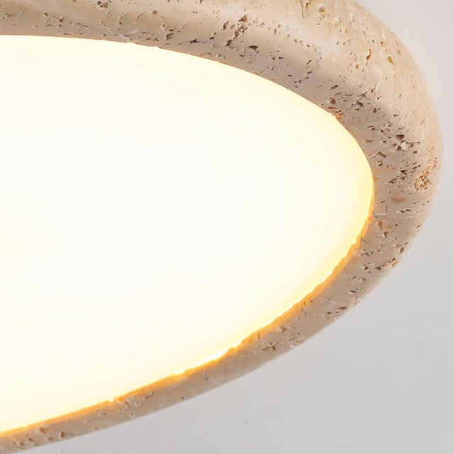 "Close-up of a modern travertine flush mount ceiling light, showcasing the texture of the natural stone frame and the soft glow of the light diffusing through the white acrylic surface."