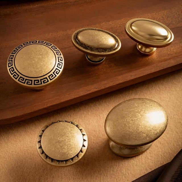 "Set of vintage-style brass cabinet knobs with intricate Grecian-inspired patterns and textured surfaces."