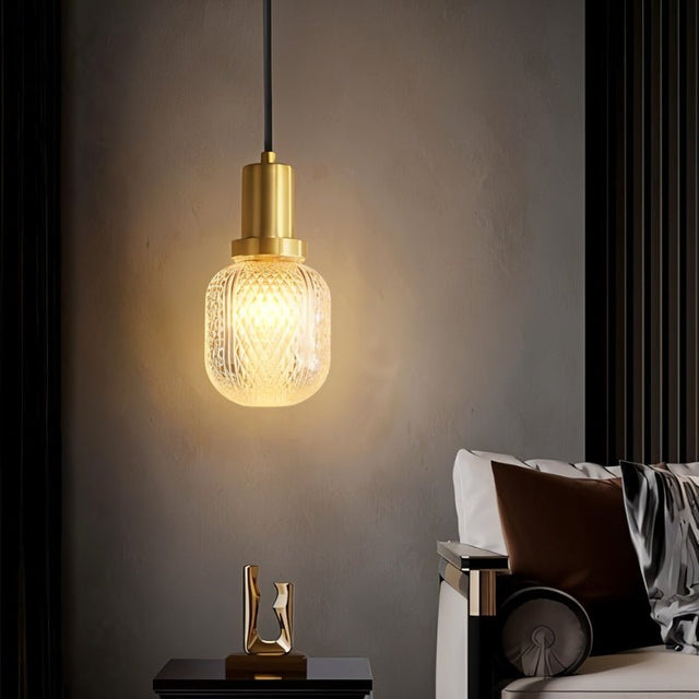 "Modern pendant light with a cylindrical brass base and a patterned, crystal-clear glass shade, creating a warm and inviting ambiance in a contemporary living room."