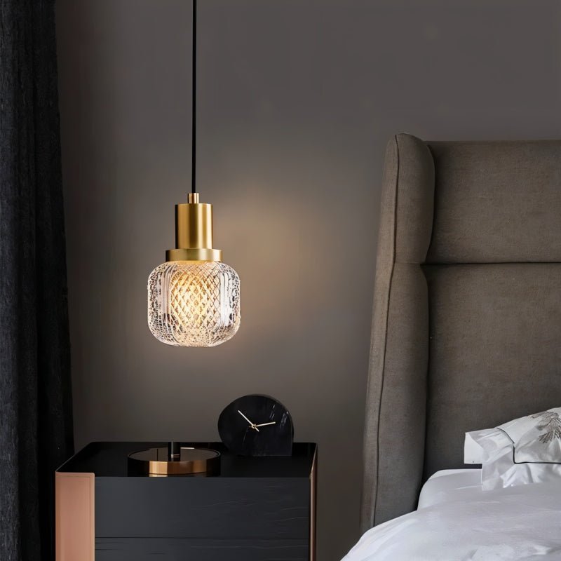 "Modern pendant light featuring a cylindrical brass base and a patterned, crystal-clear glass shade with a diamond-cut texture, diffusing light for a warm ambiance."