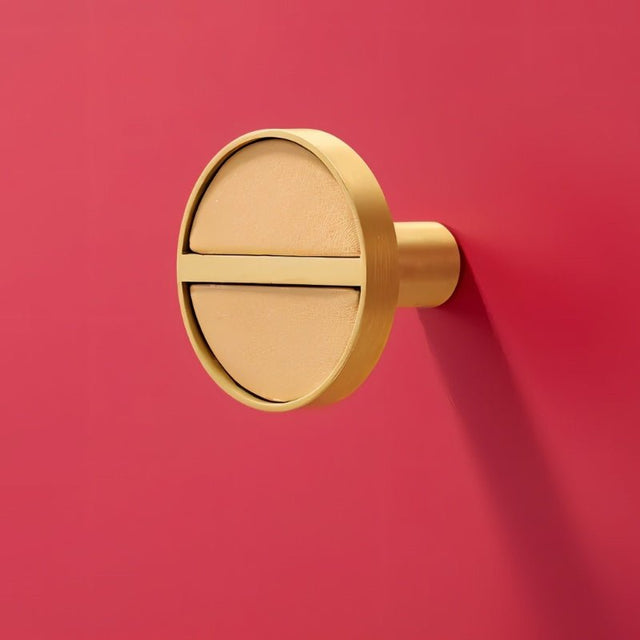 "Circular brass and tan leather cabinet knob with a modern design, combining luxury and craftsmanship."