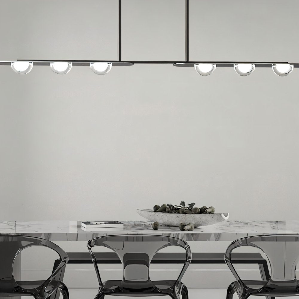 "Copper Dilti pendant light with glass globes hanging above a dining table with transparent chairs."