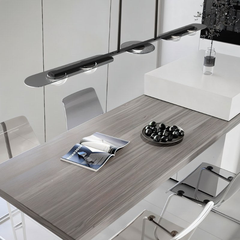 "Modern linear pendant light with silver frame and clear glass globes hanging above a dining table."