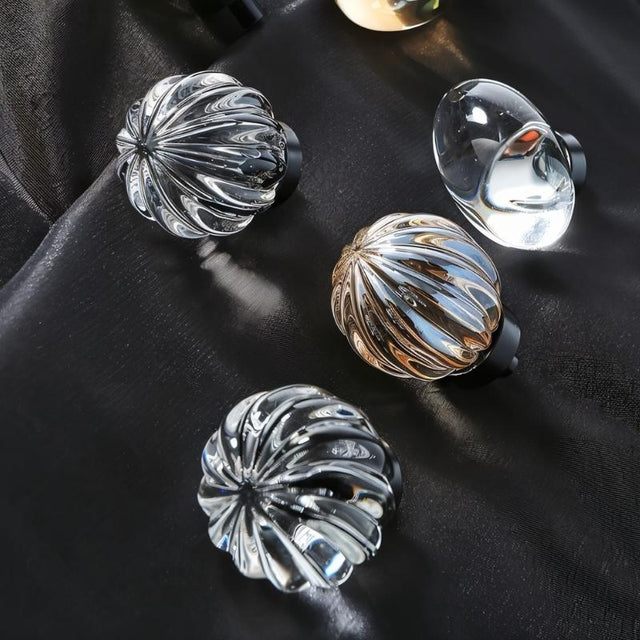 "Crystal glass knobs in spherical and oval shapes with ribbed and smooth textures on a dark fabric."