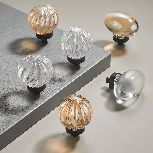 "Set of crystal glass knobs in spherical and oval shapes with ribbed and smooth textures."