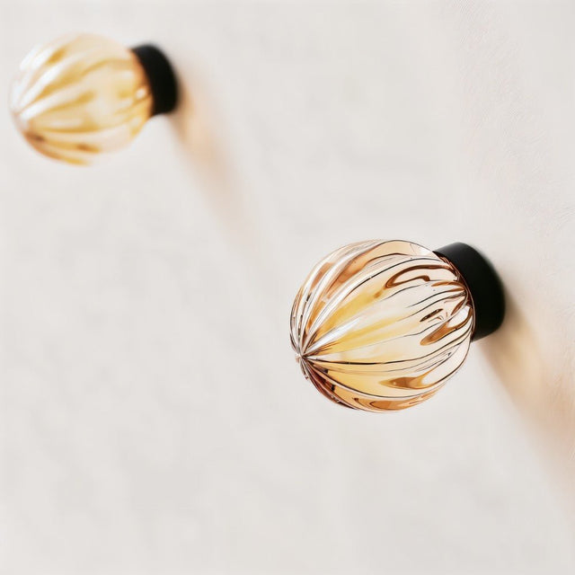 "Two amber crystal glass spherical knobs with ribbed texture on a white cabinet."