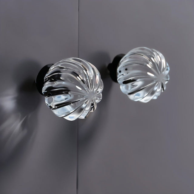 "Two clear crystal glass spherical knobs with ribbed texture on a gray cabinet."