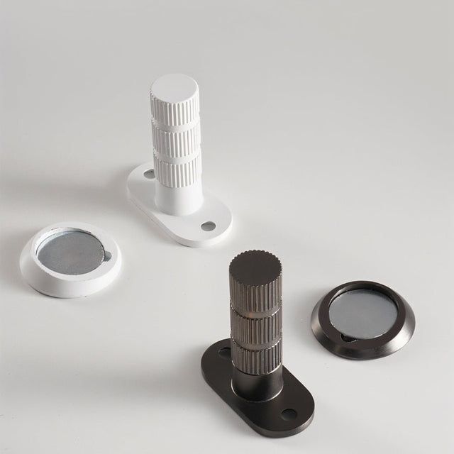"Modern magnetic door stops with textured cylindrical posts and oval mounting plates in white and brushed nickel finishes."
