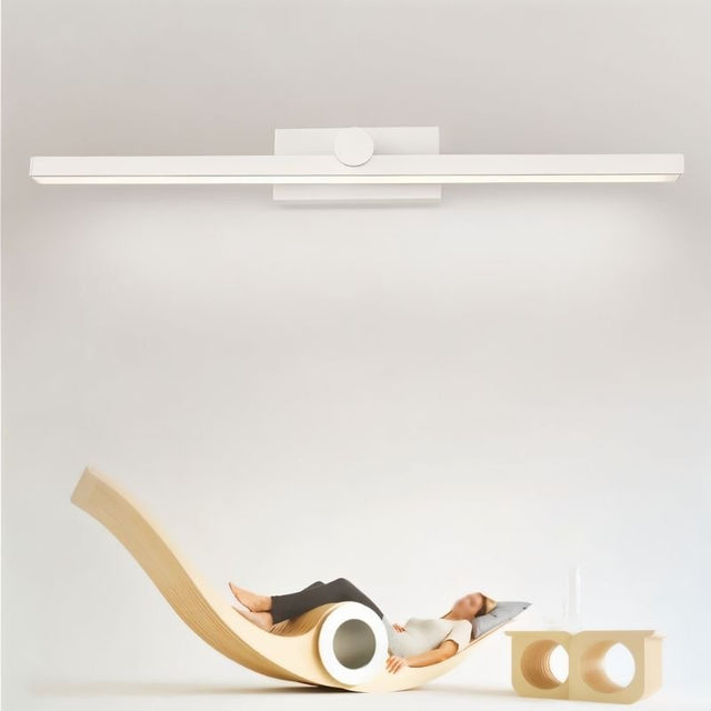 "A white wall lamp with a minimalist linear design mounted above a person reclining on a curved wooden chair in a modern, minimalist interior."