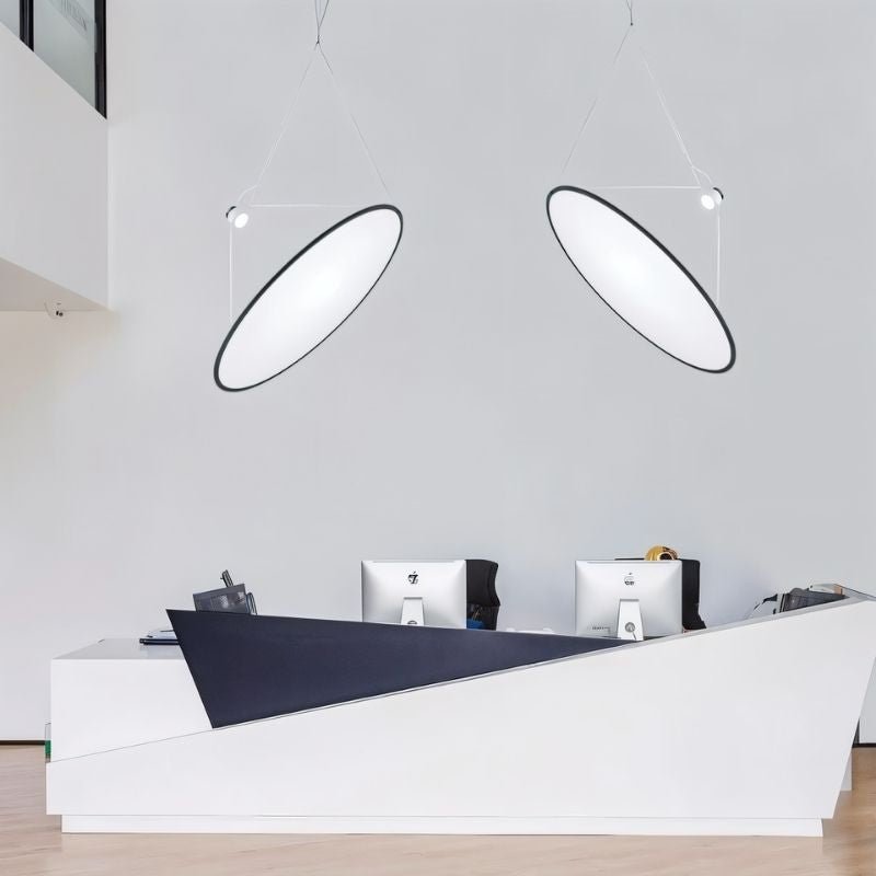"Two disc-shaped pendant lights suspended above an office reception desk, providing directional and task lighting."