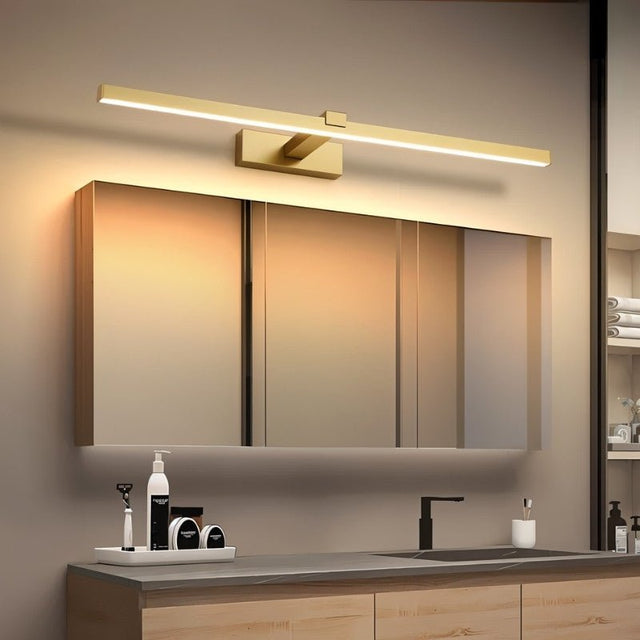 "A modern, gold LED wall lamp illuminating a bathroom vanity with a mirror and countertop."