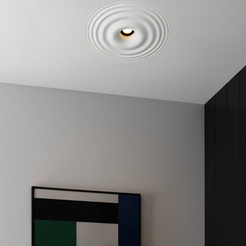 "A white ceiling light with concentric circles, installed flush in a white ceiling above a modern artwork, showing a close-up view."