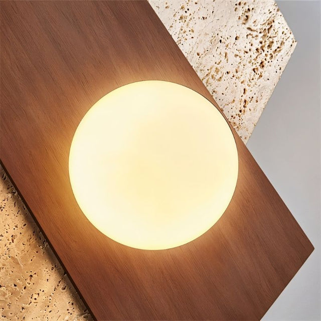 "Detailed close-up of the Eldis Wall Lamp, focusing on the warm diffused light it emits, framed by angular travertine and walnut."