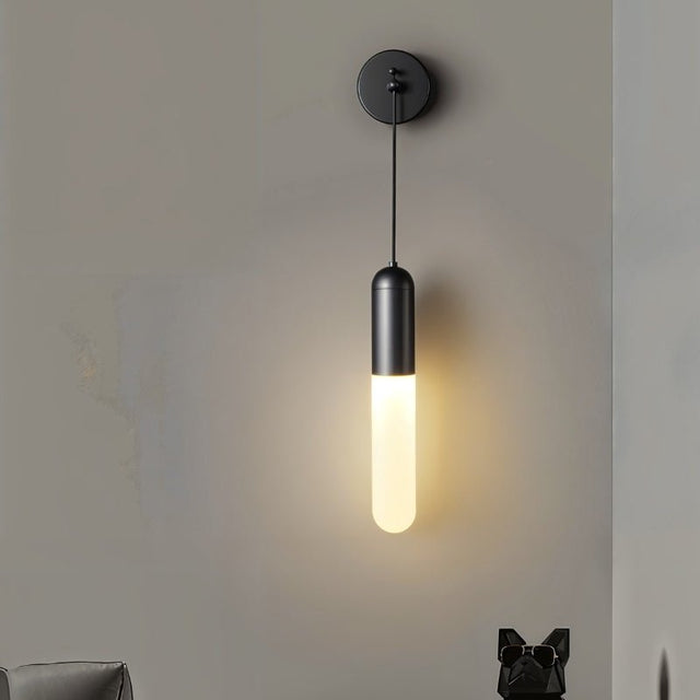 "A minimalist black wall sconce with a long, slender cylindrical shade casting a soft, warm light on a gray wall."