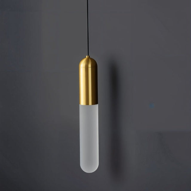 "A modern brass pendant light with a frosted, elongated cylindrical shade hanging against a dark gray background."