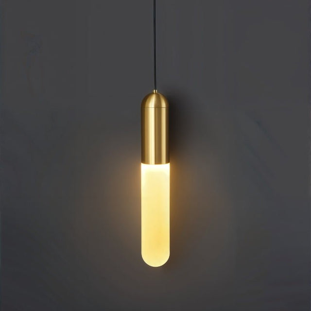 "A minimalist brass pendant light with a long, slender cylindrical shade casting a soft, warm glow against a dark gray background."