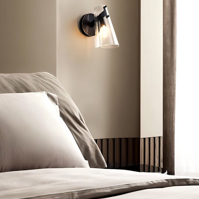 "A modern brass wall lamp with a clear acrylic shade in a bedroom setting."