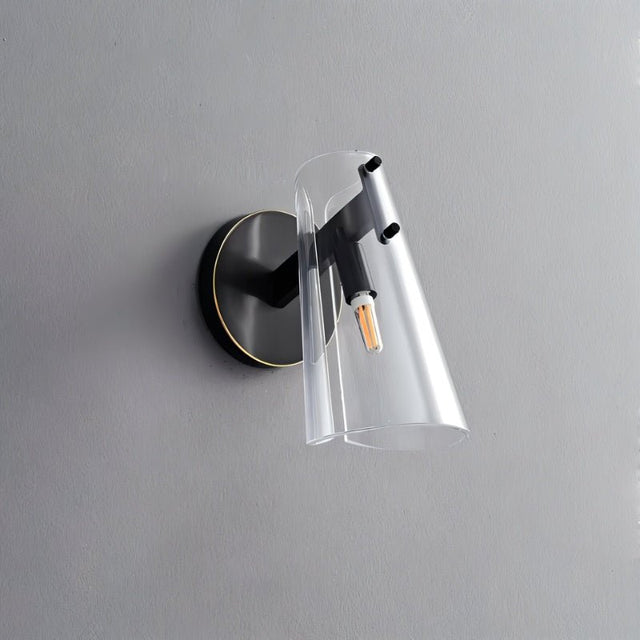 "A modern brass wall lamp with a clear acrylic shade on a gray textured wall."