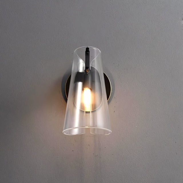 "A modern brass wall lamp with a clear acrylic shade on a gray wall."