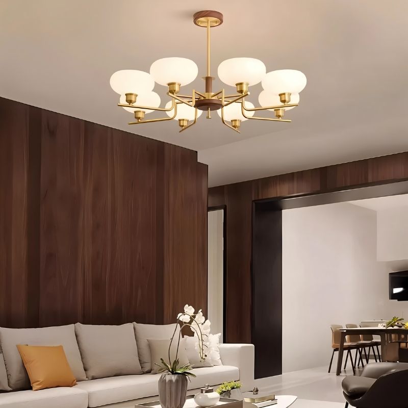 "Brass and wood chandelier with six white globe-shaped glass shades, hanging in a modern living and dining area with a sofa and dining set."