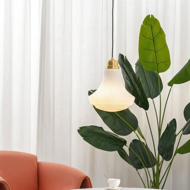"Retro pendant light with a bell-shaped, striped glass shade and brass accents in a living room setting, casting a soft, inviting glow near a large indoor plant."