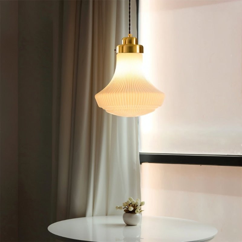 "Retro pendant light with a bell-shaped, striped glass shade and brass detailing, creating a warm, inviting ambiance above a round table with a small floral arrangement."