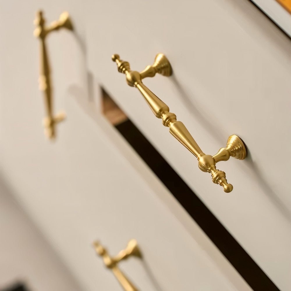 "Ornate brass pull bar handles with a classic design on light-colored drawers."