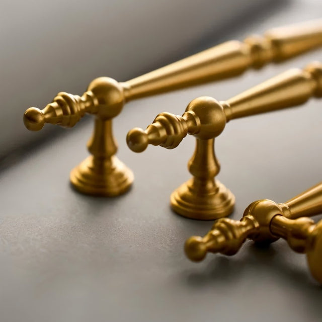 "Set of ornate brass knobs and pull bar handles with a classic design on a grey surface."