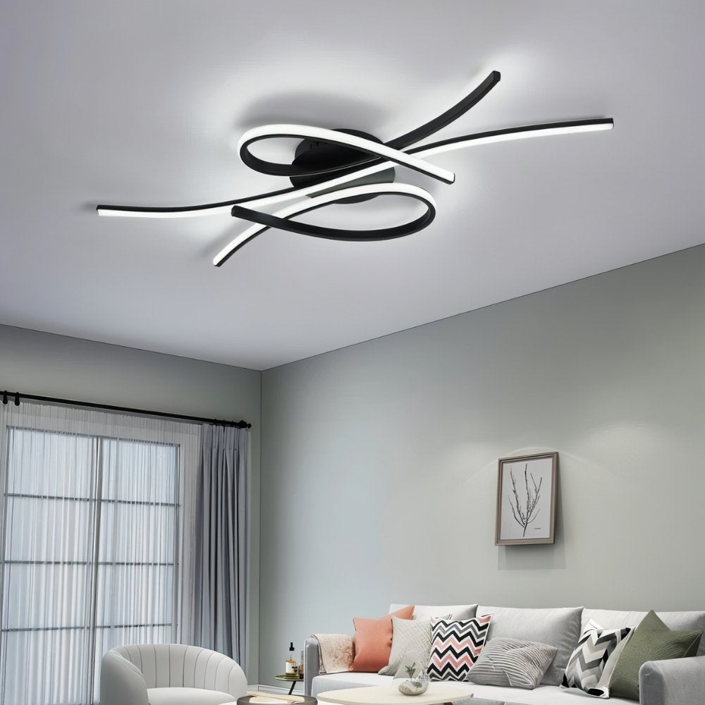 "A modern black and white ceiling light with intertwining LED bars installed in a contemporary living room with gray walls and a sofa."