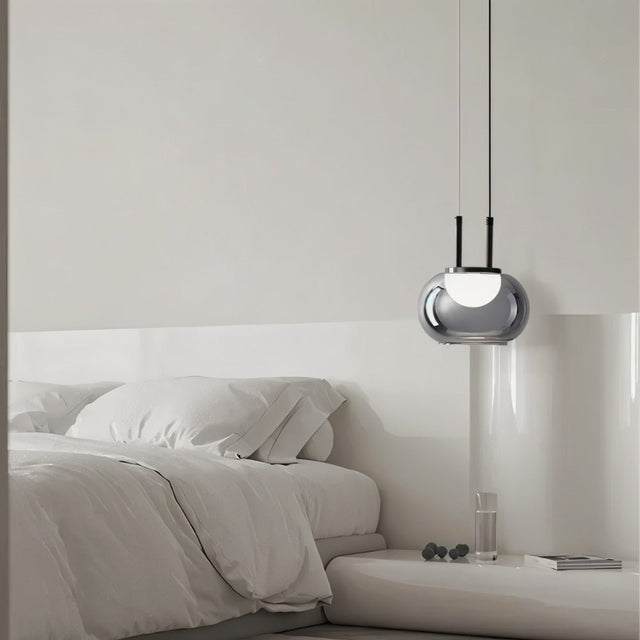 "Smoky grey Filano pendant light with a smooth glass shade and iron frame, hanging above a bed in a minimalist bedroom."