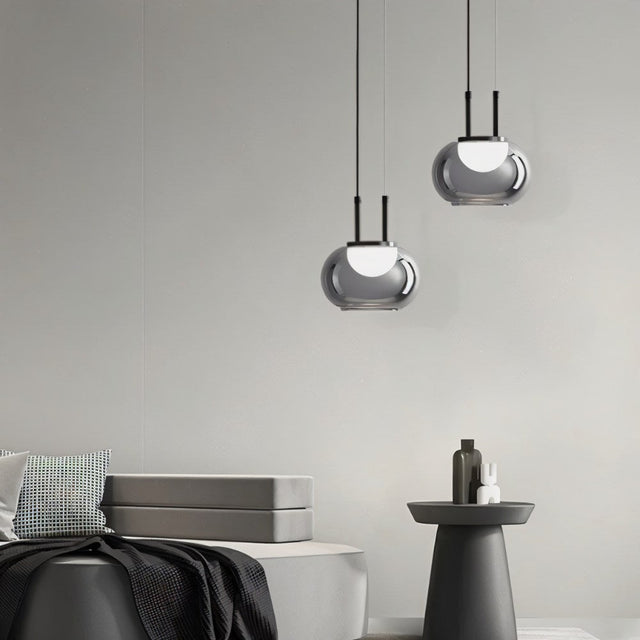 "Two smoky grey Filano pendant lights with ribbed glass shades and iron frames, hanging in a modern interior with a sofa and side table."