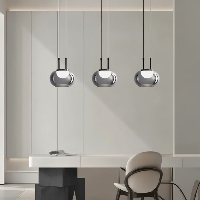 "Three smoky grey Filano pendant lights with smooth glass shades and iron frames, hanging above a desk in a modern interior."
