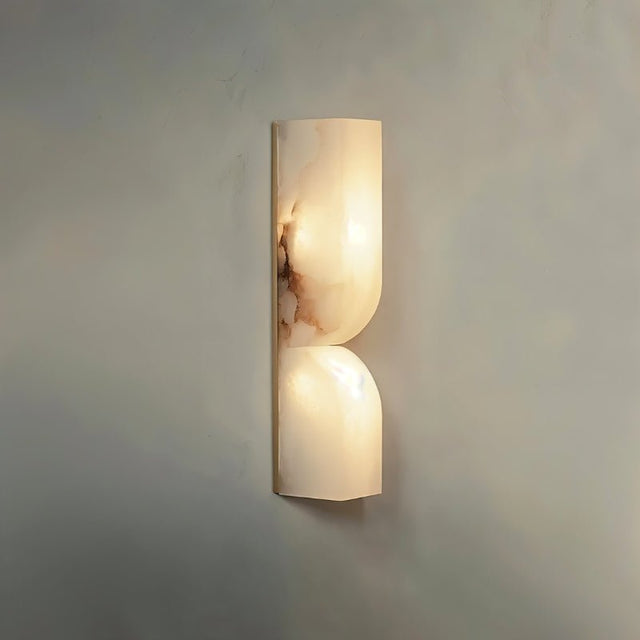 "A double-curved alabaster wall sconce emitting a soft, warm light."