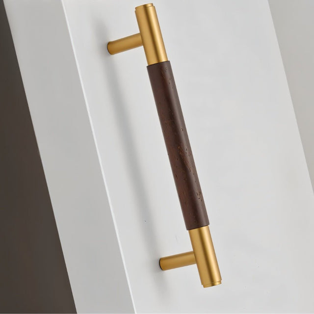 "Angled view of a wood and brass pull bar with cylindrical design on a white surface."