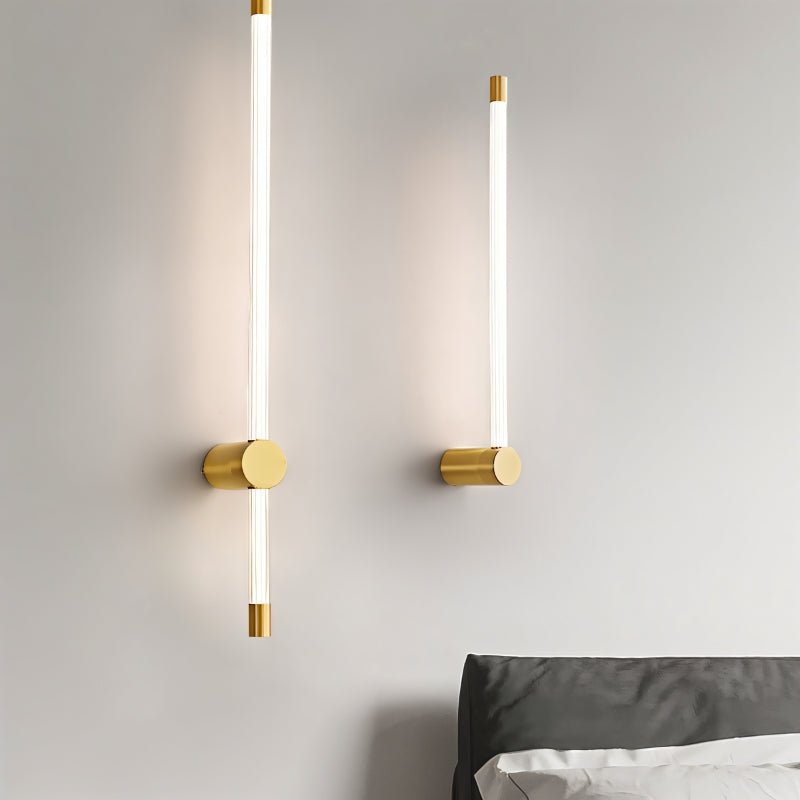 "Two modern wall sconces with long, thin light bars and brass accents, mounted on either side of a bed in a minimalist bedroom."