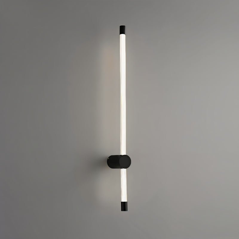 "A sleek, vertical black wall sconce with a long, thin light bar and acrylic diffuser, mounted on a gray wall."