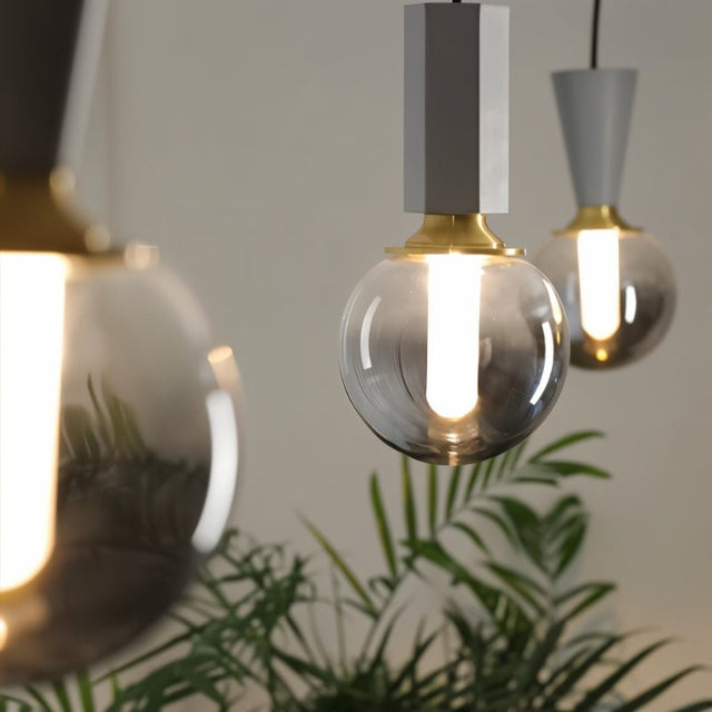 "Close-up of modern pendant lights with concrete, metal, and smoky glass orbs, highlighting the textures and warm light diffusion."