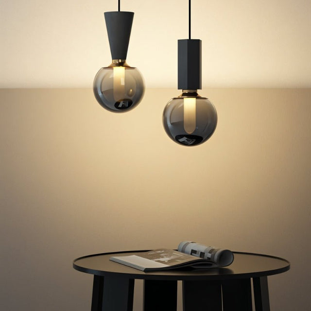 "Modern pendant lights with concrete, metal, and smoky glass orbs, creating a stylish ambiance above a contemporary table."