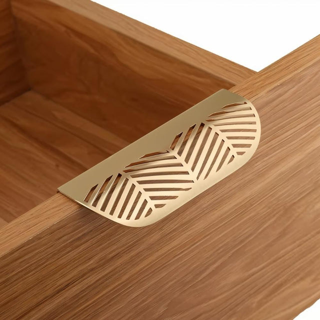 "A gold leaf-shaped drawer pull on a light wood drawer."