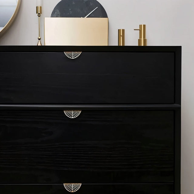 "Gold leaf-shaped drawer pulls on a black dresser in a modern bedroom."