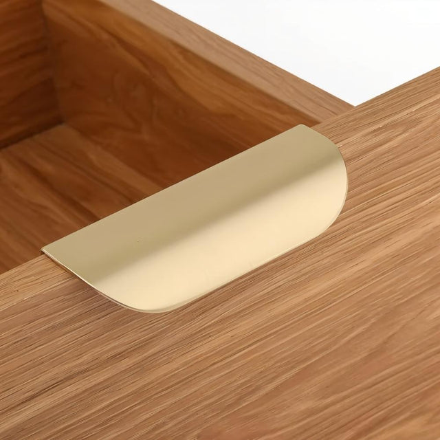 "A minimalist gold drawer pull on a light wood drawer."