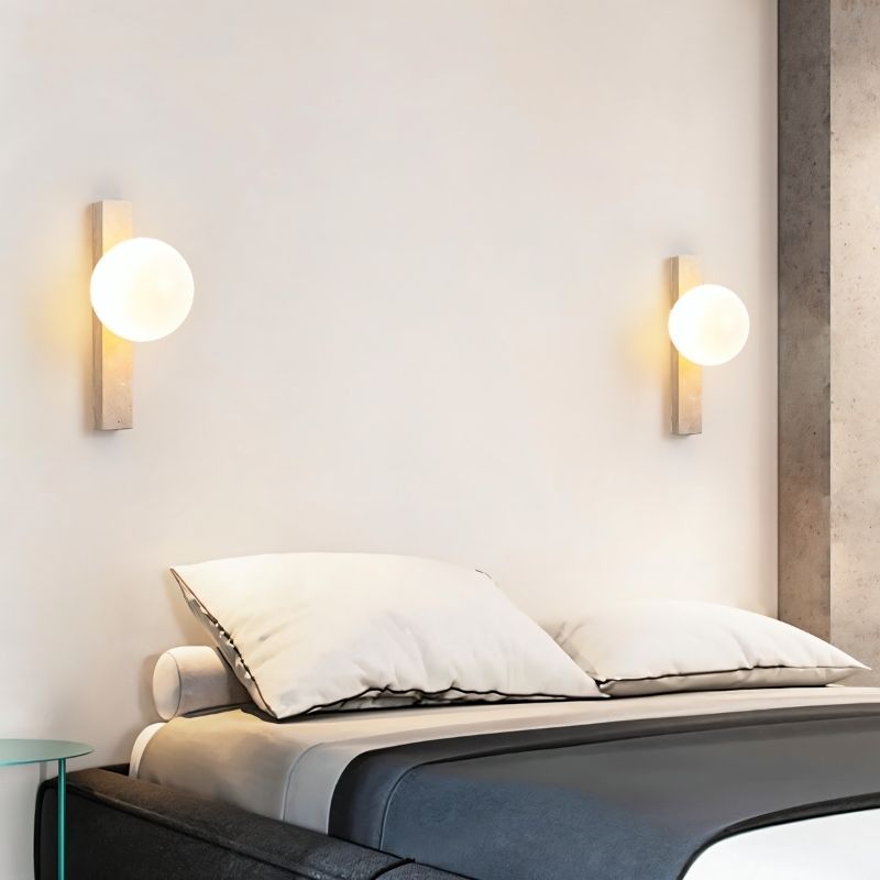 "Modern travertine wall lamps with frosted glass globes installed on both sides of a bed"