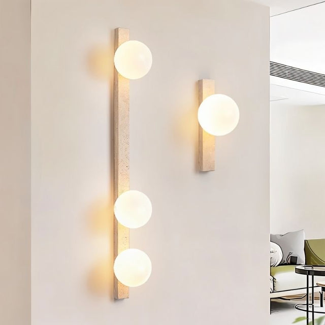 "Different sizes of travertine wall lamps with frosted glass globes installed in a modern home"