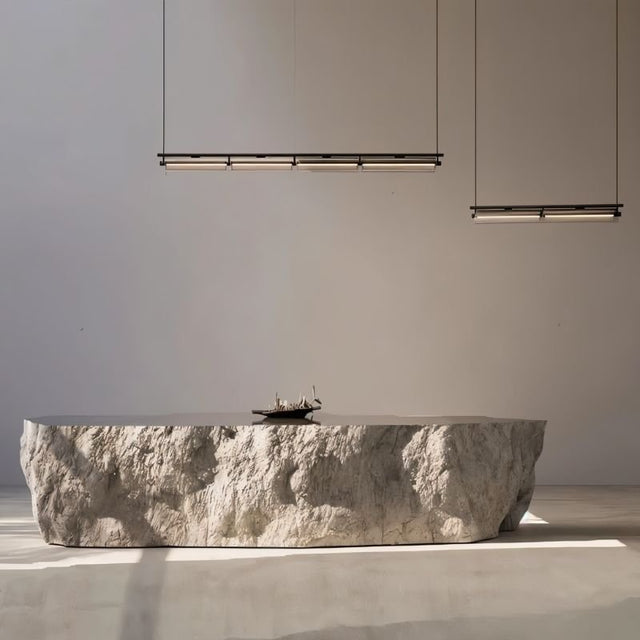 "Two modern linear pendant lights hanging above a rough-textured stone table in a minimalist interior space."