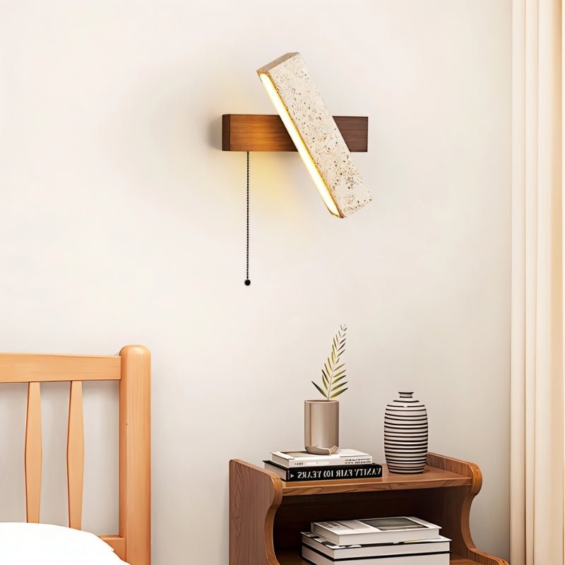 "A modern wall lamp with an angled yellow travertine shade and a walnut rectangular base, mounted on a white wall in a bedroom, casting a warm, ambient light."