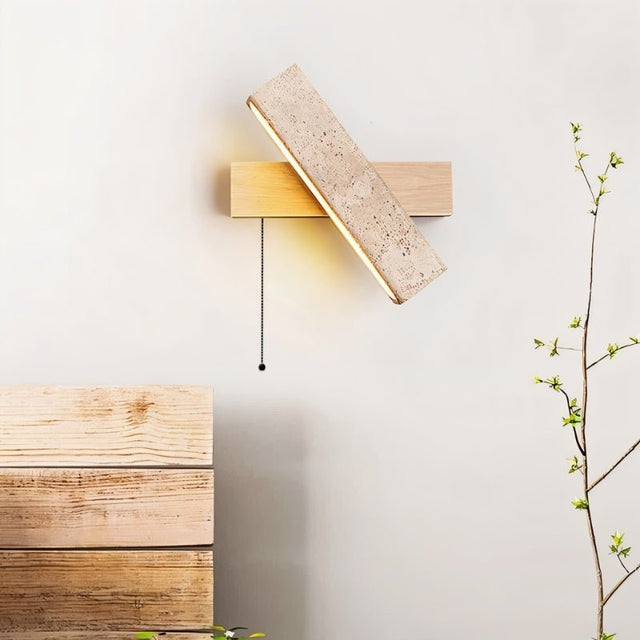 "A modern wall lamp with an angled yellow travertine shade and a light wood rectangular base, mounted on a white wall, emitting a soft, warm light in a minimalist setting."
