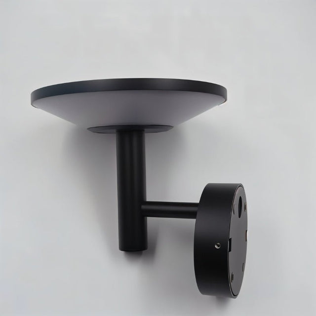 "Side view of a modern black outdoor wall lamp with a circular design, mounted on a gray wall."
