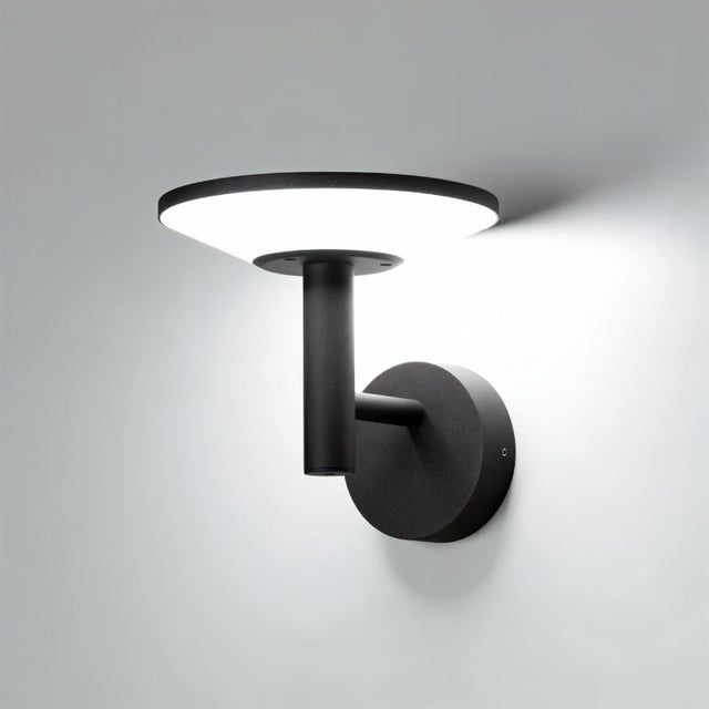 "A modern, circular outdoor wall lamp casting a bright light on a gray wall at night."