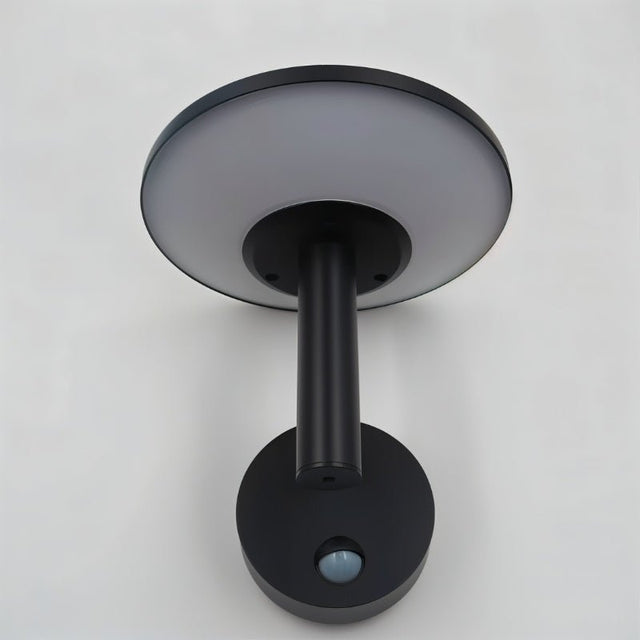"A modern, circular outdoor wall lamp with a motion sensor, mounted on a light gray wall."
