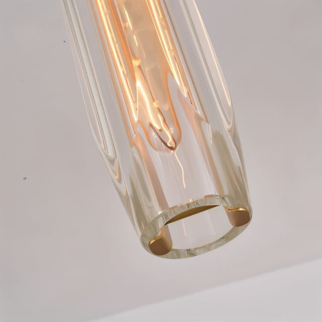 "Close-up of a modern pendant light with an elongated, faceted crystal shade and brass frame, showcasing its intricate design and captivating light refraction."